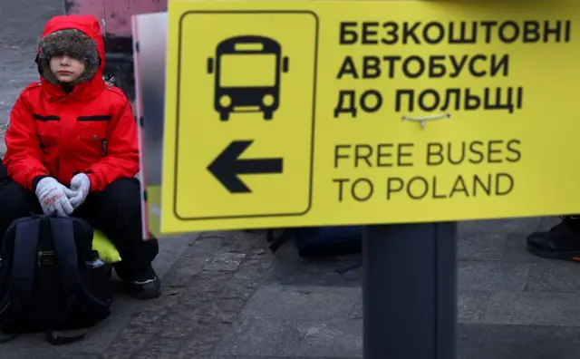 Украинский мальчик рядом с табличкой “Автобус до Польши” на украинском и английском языках