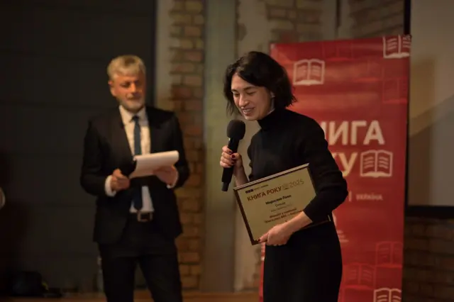 Жінка з чорним волоссям і відзнакою у руках