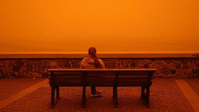 Женщина сидит на скамейке, в то время как Крит находится под покровом Сахарской пыльной бури в Греции 1 апреля 2026 года.