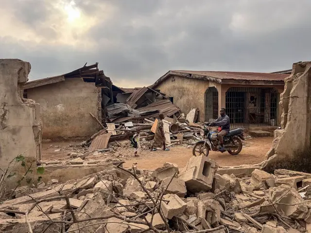 Residents and a motorcyclist move between destroyed structures in Offa on December 27, 2025 caused by debris from expended munitions that fell from US strikes on unspecified militants linked to the Islamic State group in Nigeria.