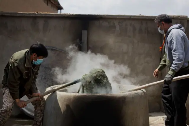 دو مرد در حال رنگ کردن تارهای قالین در یک دیگ داغ 