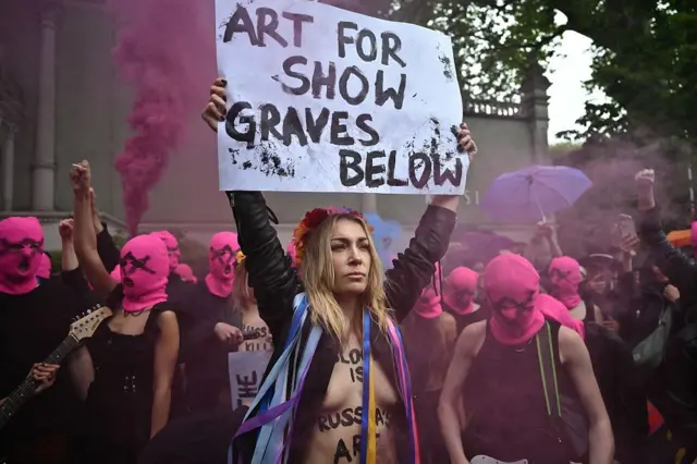 Участница Femen Инна Шевченко стоит с плакатом «Искусство напоказ, могилы под ногами» перед павильоном России, 6 мая 2026 года