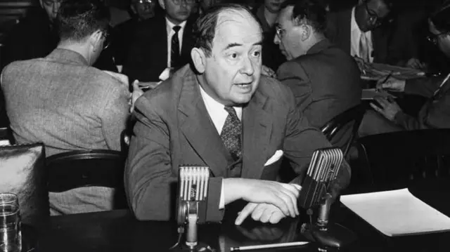 جان فون نویمان، فیزیک‌دان، ریاضی‌دان، اقتصاددان و دانشمند علوم رایانه، پشت دو میکروفون نشسته در حال سخنرانی