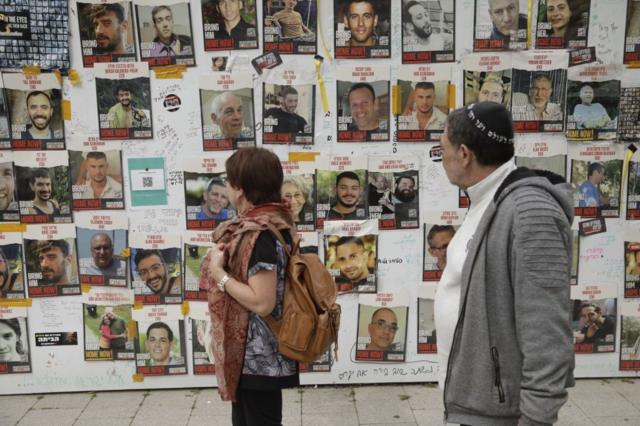 Pedestres observam cartazes de reféns israelenses em um muro em Tel Aviv, 12 de fevereiro de 2024