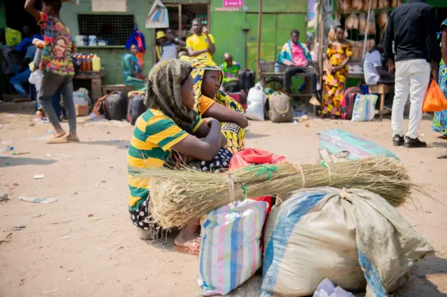 Abagore babiri bicaye barindiriye imiduga iduga ruguru ku gituro ca Cotebu i Bujumbura, 28 Nyakanga 
