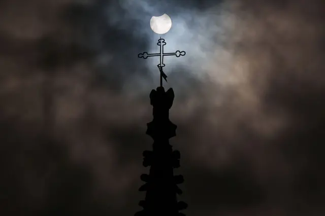 برج کلیسا به همراه صلیب بالای آن در کنار خورشید نیمه روشن