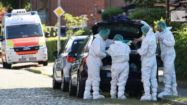 住宅街の道路脇で、黒い車のトランクが開けられ、法医学用の防護服を着た捜査官が4人、中を覗き込んでいる