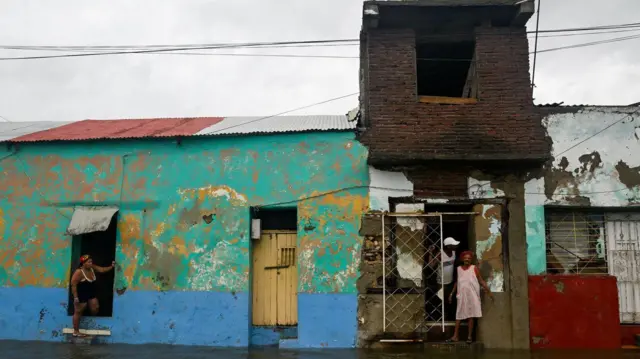 Troje ljudi stoji na dovratku uronule jednospratne kuće, oko njih je svuda voda