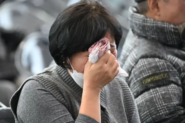 Una mujer del colectivo de familiares de víctimas del accidente de Jeju Air se seca las lágrimas con un pañuelo.