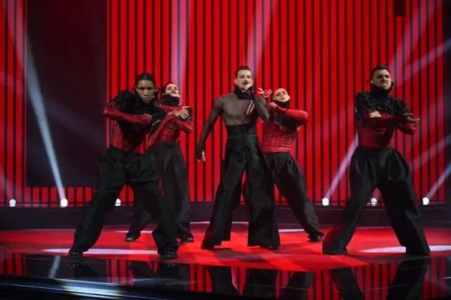 Певач у црним панталонама окружен плесачима