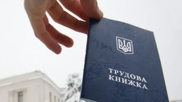 Чоловік високо тримає у руці трудову книжку. На задньому плані видніється будівля Верховної Ради.