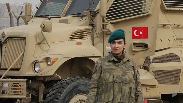 Üniformalı yeşil bereli kadın asker bir askeri aracın önünde duruyor