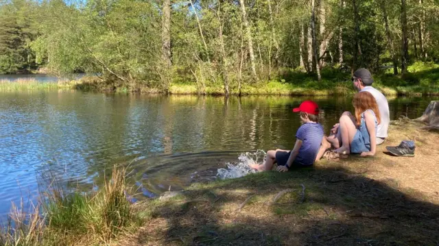 Patrick sitting and looking out across the Lake District with his children, who have their toes dipped in the water 