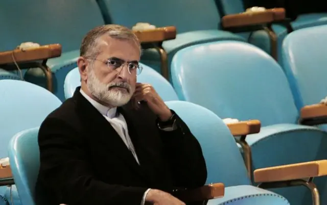 کمال خرازی در یک سالن خالی سخنرانی روی صندلی نشسته است