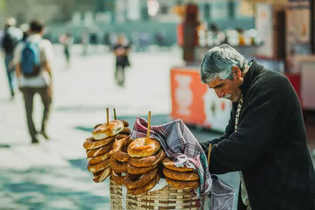 İstanbul'da simit satan yaşlı bir sokak satıcısı, simitlerin üzerindeki örtüye eğiliyor. 