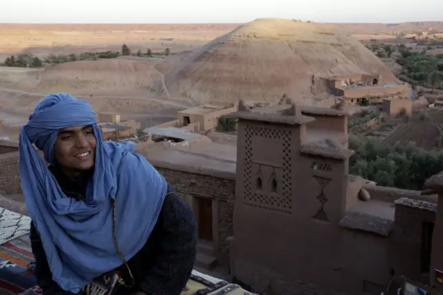 A man wearing turban sits at a rooftop cafe.