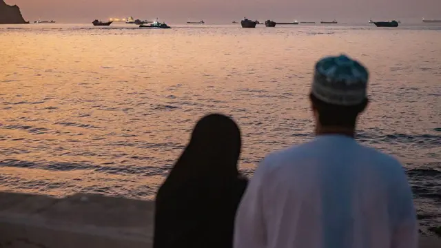 شخصان يشاهدان ناقلات نفط، وسفناً لنقل البضائع العامة، وسفناً لنقل البضائع السائبة، وقوارب صيد راسية في المياه قبالة مسقط بالقرب من مضيق هرمز، في 18 يونيو/حزيران 2026.