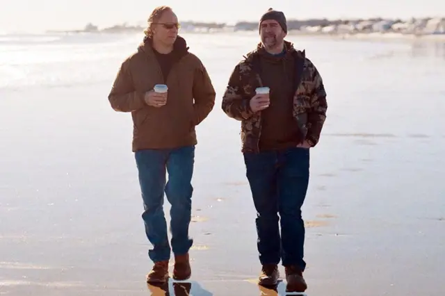 ਗ੍ਰੇਗ ਸਕੁਇਰ ਅਤੇ ਪੀਟ ਮੈਨਿੰਗ ਸਮੁੰਦਰ ਦੇ ਕਿਨਾਰੇ ਹੱਥਾਂ ਵਿੱਚ ਟੇਕ-ਅਵੇ ਡਰਿੰਕਸ ਫੜ ਕੇ ਸੈਰ ਕਰ ਰਹੇ ਹਨ