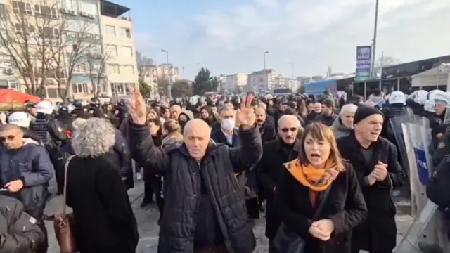 Protesto gösterisi. Öndeki bir kişi zafer işareti yapıyor.