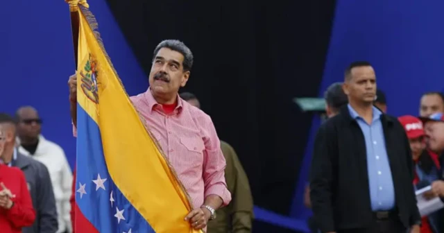 Foto mostra Nicolás Maduro empunhando uma bandeira da Venezuela. Ele veste uma camisa rosa e segura a bandeira do país olhando para cima