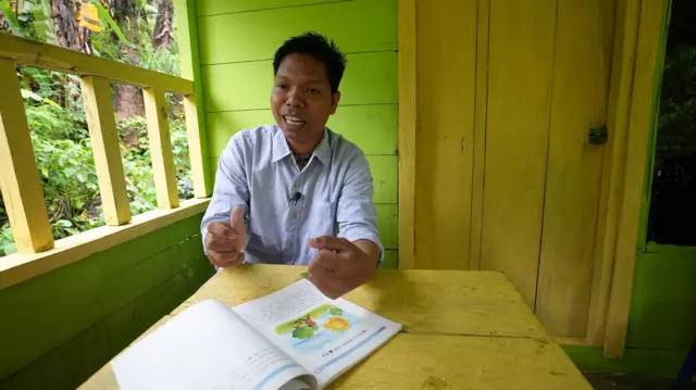 Sarianto duduk di teras rumahnya saat diwawancarai oleh BBC News Indonesia. Di meja di depannya, terletak sebuah buku cerita anak bahasa Cia-Cia yang ditulis dalam aksara Hangeul.