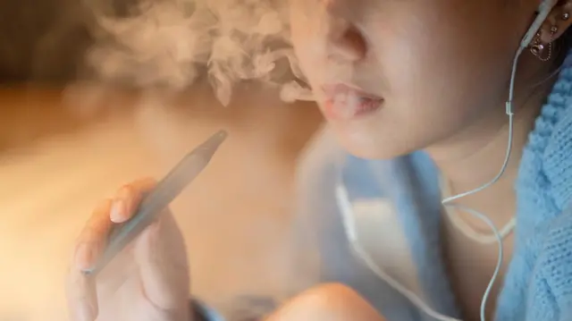 圖示呈現一名女性正在夜晚使用電子煙。