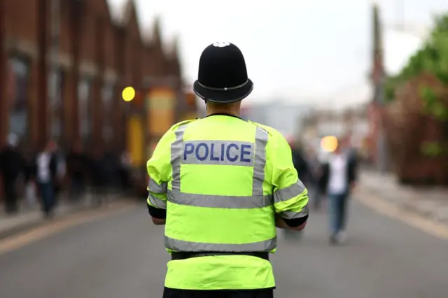 Un policía británico fotografiado de espaldas vistiendo un chaleco fluorescente amarillo.