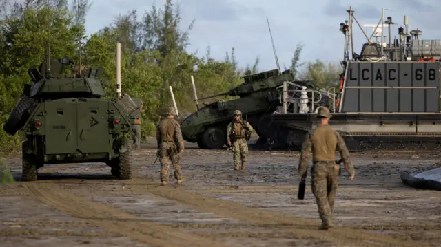 Un vehículo blindado se descarga de un vehículo anfibio LCAC de la Armada de EE. UU. durante un entrenamiento en Arroyo, Puerto Rico, el 5 de septiembre de 2025. Se ve a varios militares caminar en la playa junto a los vehículos. 