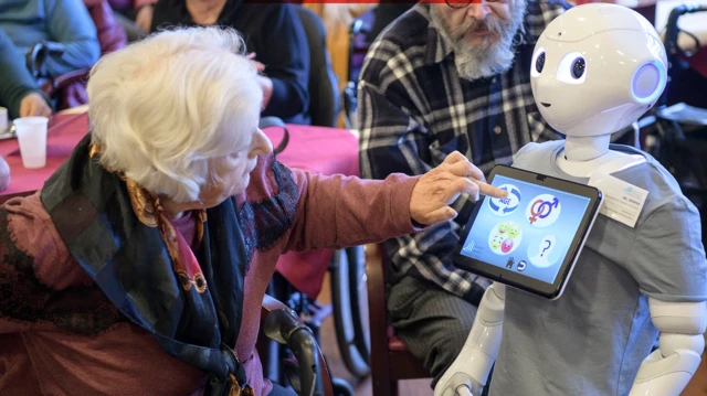 İleri yaştaki bir kadın robotun göğsündeki ekrana dokunuyor