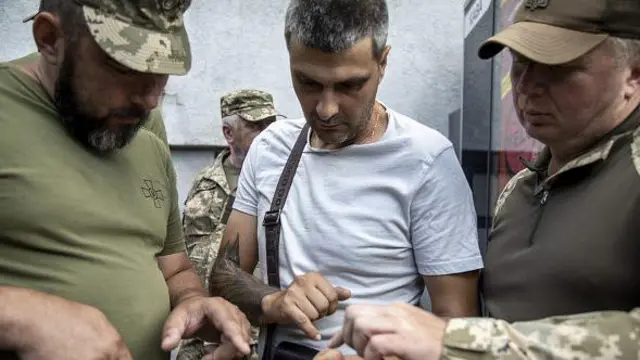 Двє співробітників ТЦК перевіряють чоловіка на вулиці Харкова