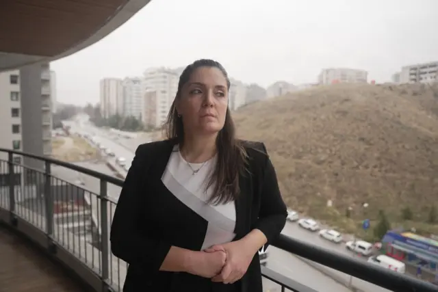 Sıdıka Akdeniz'in balkonda çekilmiş fotoğrafı. Üzerinde siyah ve beyaz renkli bir kıyafet var. Akdeniz, Ankara'daki diş kliniğinin balkonundan dışarıyı izliyor.