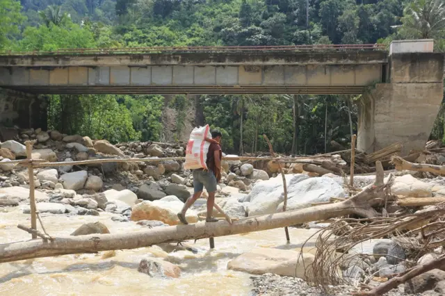 Warga meniti jalan pada pohon saat melintasi Desa Pepelah, Kecamatan Pinding, Kabupaten Gayo lues, Aceh, Senin (22/12/2025).