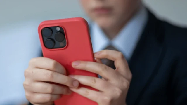 پسری که چهرهاش پیدا نیست یک موبایل قرمز در دست دارد