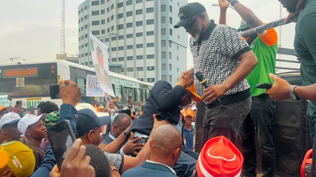 Dino Melaye holding micas e dey drag Amaechi up, pipo surround am