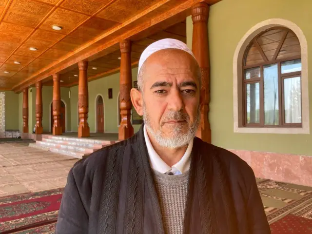 Imam Saidrahman Habibov pictured inside a mosque with wooden pillers and prayer mats on the floor