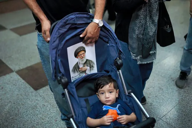 Seorang pria mendorong kereta bayi yang dipasang potret Ali Khamenei, saat warga berdatangan ke sebuah stasiun menjelang prosesi pemakaman Khamenei dan sejumlah anggota keluarganya.