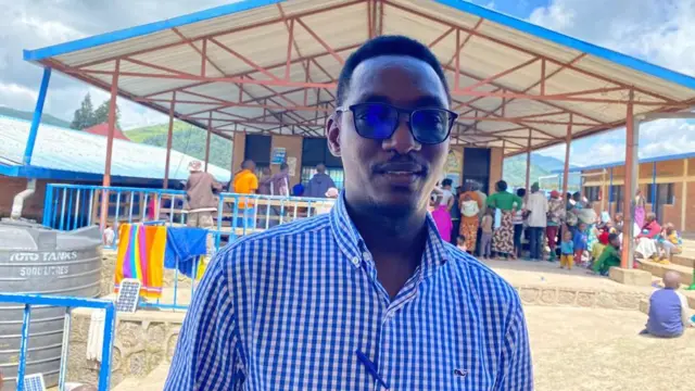 Umugabo wambaye ishati ya karo karo y'ubururu n'umweru, yambaye indorerwamo ndetse yashyize ikaramu iruhande rw'igifungo cy'ishati ye