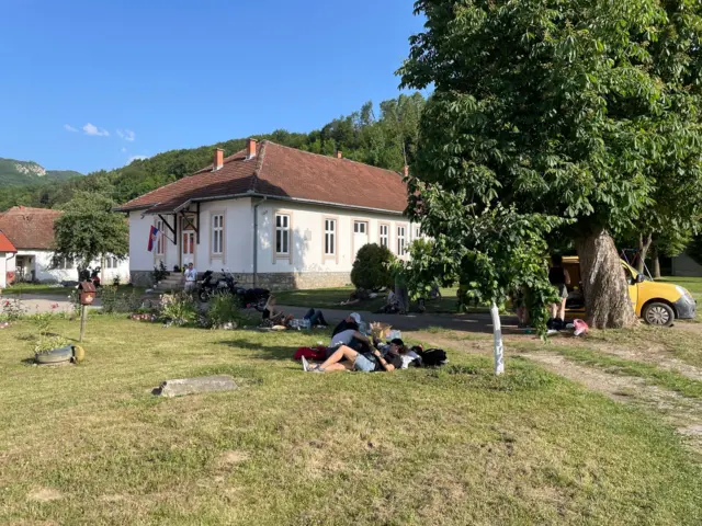 Ljudi leže na travnjaku u blizini kuće u kojoj se glasa