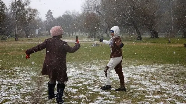 Monde Sussman (L) take a picture of Gabriel Sussman (R) as snow falls in Zoo Lake park in Johannesburg on July 10, 2023. 