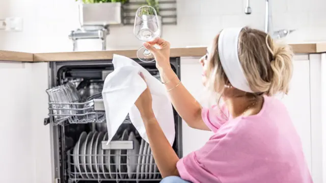 Młoda kobieta w domu sprawdza, czy szklanka, którą umyto w zmywarce, lśni