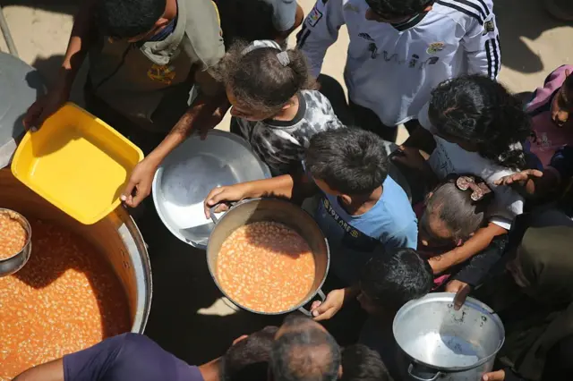 Palestinos con ollas y contenedores se reúnen mientras una organización benéfica distribuye alimentos en Az-Zawayda, Deir al-Balah, Gaza, donde el acceso a los alimentos sigue siendo difícil debido al bloqueo y los ataques constantes de Israel.
