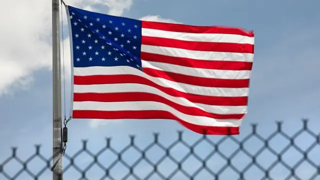 Bandeira dos Estados Unidos hasteada e tremulando atrás de uma cerca