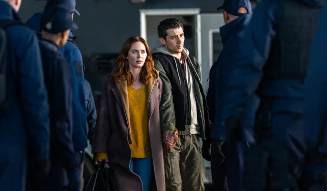 Kard z filmu Dzień objawienia. Na środku zwróceni twarzami do obiektywu kobieta i mężczyzna, otoczeni przez osoby w niebieskich mundurach. 