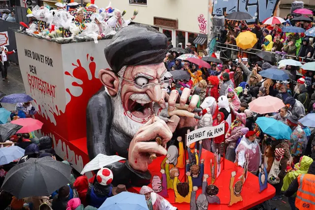 مجسمه آیت الله خامنهای با چهره هیولا مانند. دهانش باز است و چند نفر در مقابلش تظاهرات میکنند