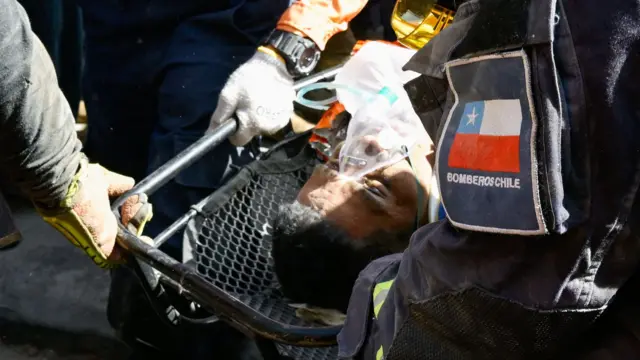Lice muškarca na nosilima i sa bocom kiseonika, okruženoh spasiocima
