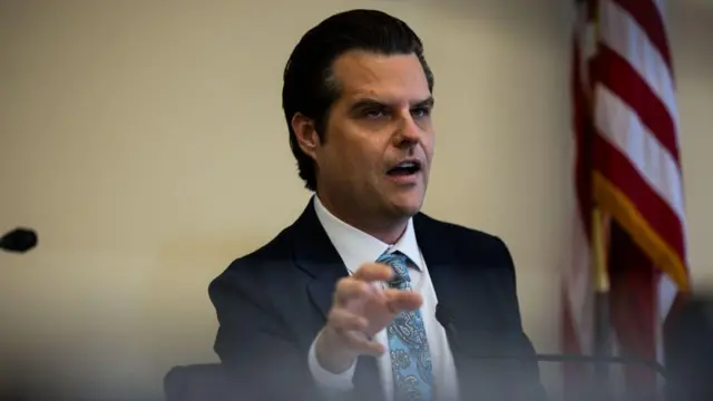 Matt Gaetz, mặc một bộ vest, chỉ tay bằng ngón tay trỏ trong khi ngồi và phát biểu vào micro trong một phiên điều trần.





