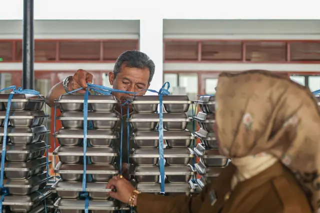 Dua staf sekolah memeriksa dan merapikan wadah makanan bergizi gratis (MBG) sebelum dibagikan kepada siswa di SMA Negeri 20 di Bandung, Jawa Barat, Indonesia, pada 14 April 2025.
