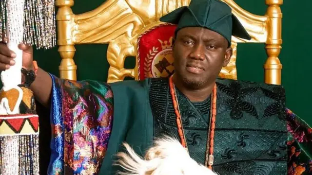 Alaafin Abimbola Owoade joko lori itẹ, o mu ọpa asẹ to ni ilẹkẹ lori lọwọ, o wọ asọ Damaski alawọ ewe ati fila abetiaja asọ Damaski naa, o si fi ilẹke sọrun pẹlu.