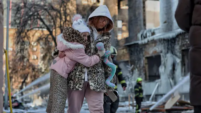 Жінка несе дівчинку з іграшкою біля зруйнованої будівлі після атаки російського дрона 12 січня в Києві