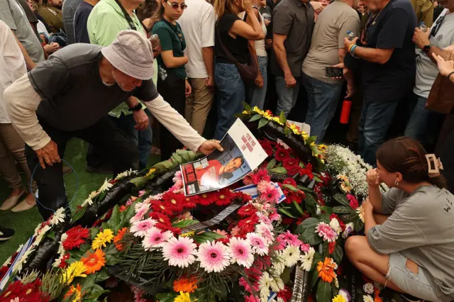 Una persona sostiene la foto de Tamir Nimrodi, un soldado israelí que murió en cautiverio en Gaza tras ser capturado en octubre de 2023, que yace sobre un montón de flores rodeado de dolientes en la ciudad central israelí de Kfar Saba.16 de octubre de 2025.